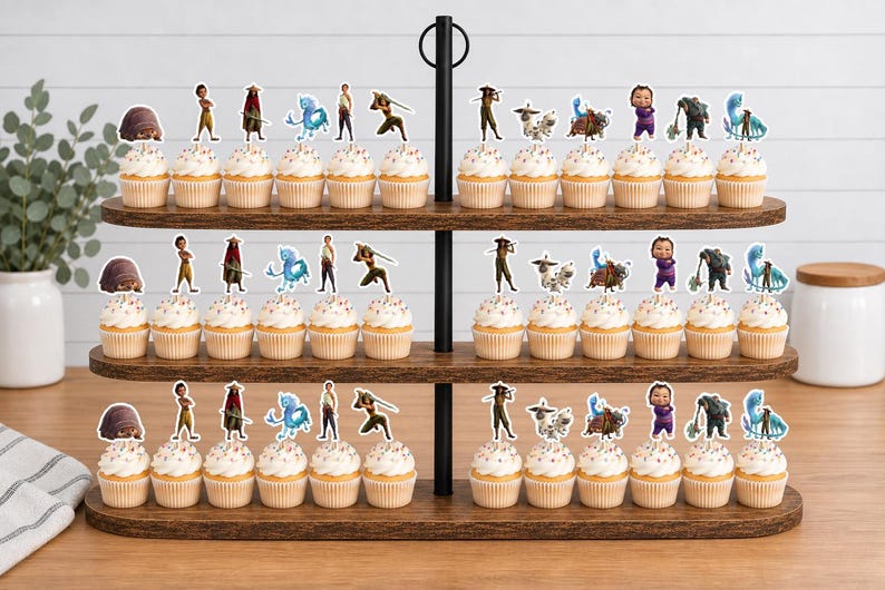 K&ouml;nnte beinhalten: Ein dreist&ouml;ckiger Cupcake-St&auml;nder aus Holz mit Cupcakes, die mit Papieraufstellern von Zeichentrickfiguren verziert sind. Die Figuren zeigen ein kleines Wesen, eine Person in Gelb, eine Person mit rotem Umhang und eine blaue Kreatur.