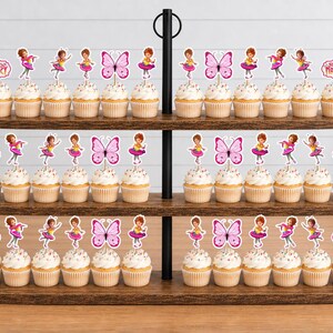 May include: A three-tiered wooden cupcake stand holding numerous cupcakes topped with decorative paper toppers. The toppers feature illustrations of a girl in a pink dress, pink butterflies, and signs with the text Fancy Nancy in pink script.