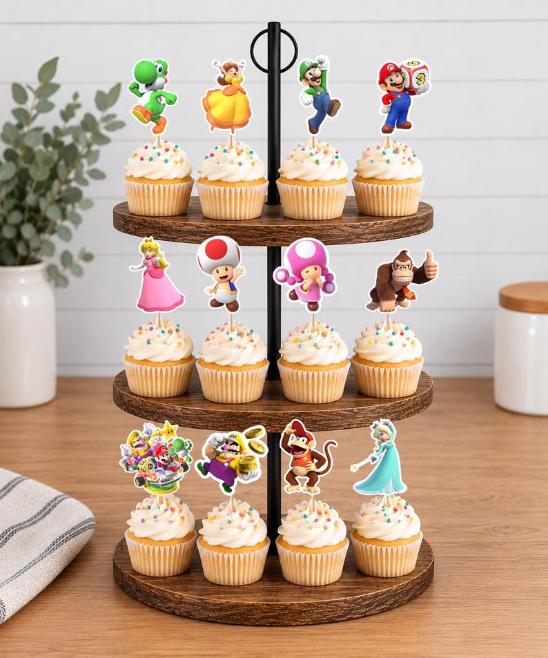 Pu&ograve; includere: Un'alzata per cupcake in legno a tre livelli che sostiene dodici cupcake guarniti con glassa bianca e zuccherini colorati. Ogni cupcake presenta un topper decorativo in carta che raffigura vari personaggi Nintendo tra cui Mario, Luigi, Peach, Toad e Donkey Kong.