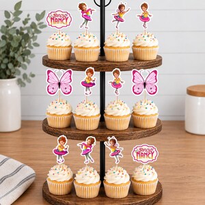 May include: A three-tiered wooden cupcake stand holding twelve cupcakes topped with colourful sprinkles. The cupcakes are decorated with paper toppers featuring the character Fancy Nancy, pink butterflies, and the text Fancy Nancy in pink and yellow.