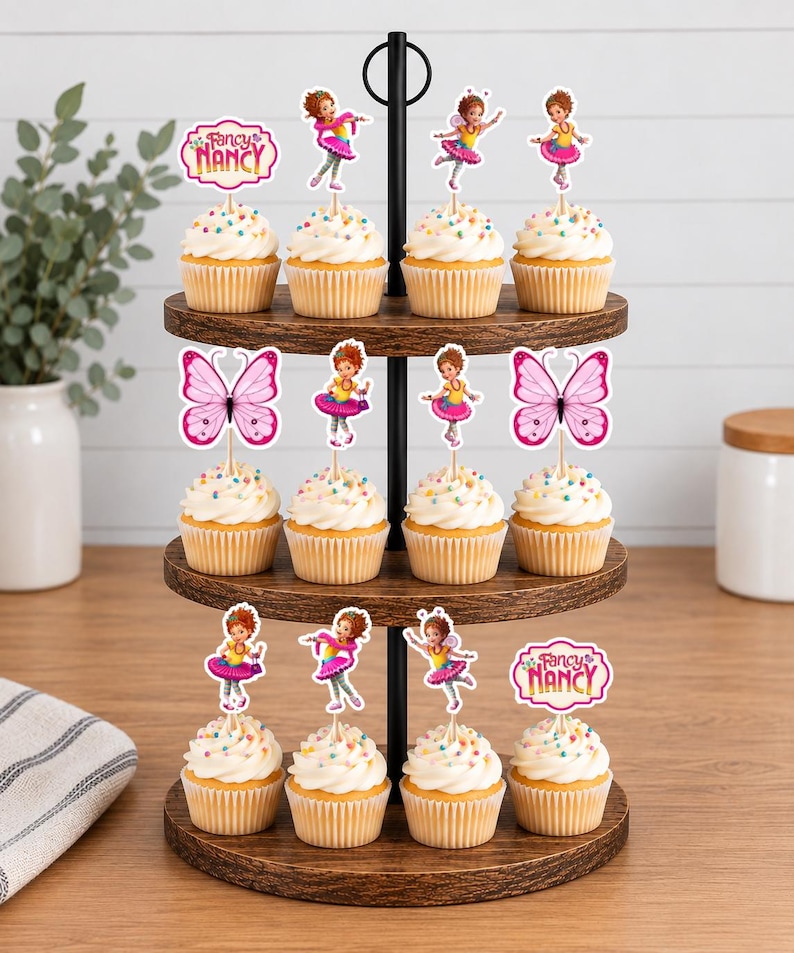 May include: A three-tiered wooden cupcake stand holding twelve cupcakes topped with colourful sprinkles. The cupcakes are decorated with paper toppers featuring the character Fancy Nancy, pink butterflies, and the text Fancy Nancy in pink and yellow.