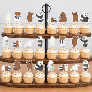 May include: A three-tiered wooden cupcake stand holding twenty-four cupcakes, each topped with a colourful sprinkle frosting and a paper cutout of characters from the animated series We Bare Bears, featuring Grizzly, Panda, and Ice Bear in various poses.