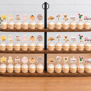 Puede incluir: Un expositor de madera de tres niveles con filas de cupcakes coronados con adornos de papel. Los adornos presentan varias ilustraciones que incluyen un sol amarillo, un pato, un pastel, un conejo, tortitas, un oso, un cruas&aacute;n y flores.