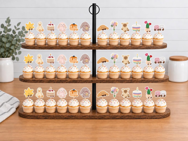 Puede incluir: Un expositor de madera de tres niveles con filas de cupcakes coronados con adornos de papel. Los adornos presentan varias ilustraciones que incluyen un sol amarillo, un pato, un pastel, un conejo, tortitas, un oso, un cruas&aacute;n y flores.