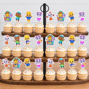 May include: A three-tiered wooden cupcake stand holding twenty-four cupcakes topped with colourful paper cutouts of cartoon characters and the text "Lucas & Friends". The cupcakes feature white frosting with multi-coloured sprinkles on paper liners.