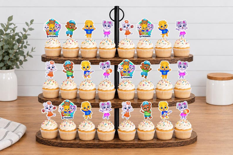 May include: A three-tiered wooden cupcake stand holding twenty-four cupcakes topped with colourful paper cutouts of cartoon characters and the text "Lucas & Friends". The cupcakes feature white frosting with multi-coloured sprinkles on paper liners.
