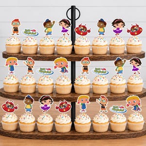 Puede incluir: Un soporte de madera para cupcakes de tres niveles con veinticuatro cupcakes decorados con adornos de papel de los Little Einsteins. Cada cupcake tiene un envoltorio de papel blanco y recortes coloridos de Leo, June, Quincy, Annie y Rocket.