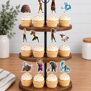K&ouml;nnte beinhalten: Ein dreist&ouml;ckiger Cupcake-St&auml;nder aus Holz mit zw&ouml;lf Cupcakes, die mit wei&szlig;em Zuckerguss und bunten Streuseln verziert sind. Jeder Cupcake hat einen dekorativen Papieraufsatz, der verschiedene animierte Figuren aus dem Film Raya und der letzte Drache zeigt.