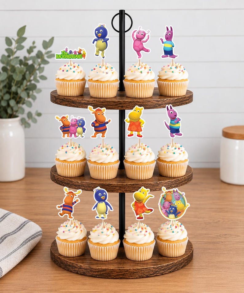 May include: A three-tiered wooden cupcake stand holding twelve cupcakes topped with white frosting and colorful sprinkles. Each cupcake features a paper topper depicting characters from The Backyardigans, including Pablo, Tyrone, Uniqua, Tasha, and Austin.