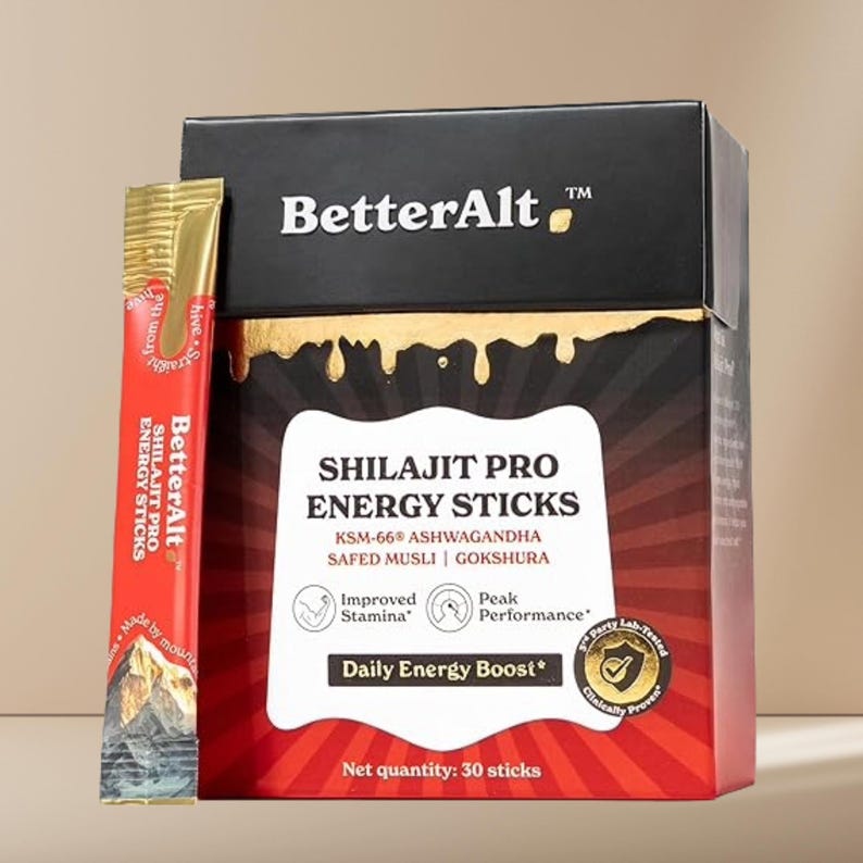 Puede incluir: Una caja de producto y un solo stick de BetterAlt Shilajit Pro Energy Sticks. La caja es negra y roja con detalles dorados y el texto "Shilajit Pro Energy Sticks" y "Daily Energy Boost". El stick es rojo y dorado.