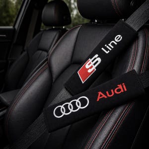 Pode incluir: Almofadas pretas para cintos de segurança com o logotipo da Audi e o texto "S Line" em branco e vermelho. As almofadas estão em um assento de carro preto com costuras vermelhas.