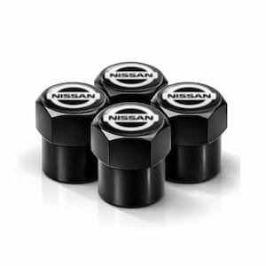 Peut inclure: Quatre bouchons de valve noirs avec le logo Nissan en blanc. Les bouchons ont une forme hexagonale et une base cylindrique. Le logo Nissan est centré sur un fond blanc.