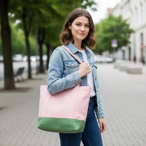 May include: A pink and green tote bag with a rectangular shape. The top portion of the bag is pink, and the bottom is green. The bag has a shoulder strap and is being carried by a person.