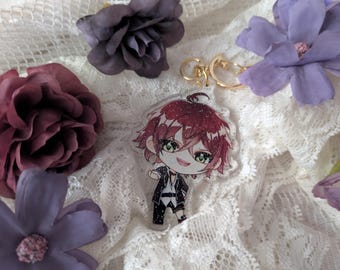 Puede incluir: Un llavero de acrílico transparente con un personaje estilo chibi de cabello rojo puntiagudo, ojos verdes y un atuendo en blanco y negro. El diseño presenta un acabado con purpurina y está unido a una argolla de metal dorado.