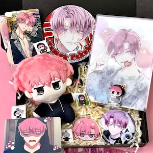 May include: A pink-haired anime character-themed gift box. The box contains a plush doll, acrylic charms, a button, and several cards featuring the character. The items are arranged on decorative paper.