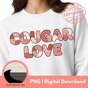 May include: White sweatshirt with the words "COUGAR LOVE" in a patchwork style, using shades of pink and red. The text is the focal point, with a copyright stamp in the upper right corner. The bottom of the image includes a logo and text.