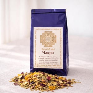 Op de afbeelding: Een donkerblauwe theezak met gouden tekst en een geometrisch ontwerp. De zak is gelabeld met "Bilkov Chai Chakra" in Cyrillisch schrift. Losse theebladeren, waaronder rozenblaadjes en zaden, zijn voor de zak verspreid.