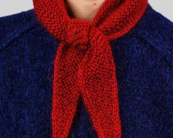 May include: A close-up of a red knitted scarf tied around a person's neck. The scarf is a vibrant red color and has a textured appearance. The person is wearing a dark blue jacket with a silver zipper.