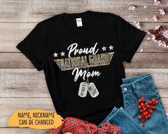 May include: Black t-shirt with the text "Proud National Guard Mom" in white script and a camouflage design. Includes two dog tags with the name "Wyatt". The shirt is paired with blue jeans and a red plaid shirt.