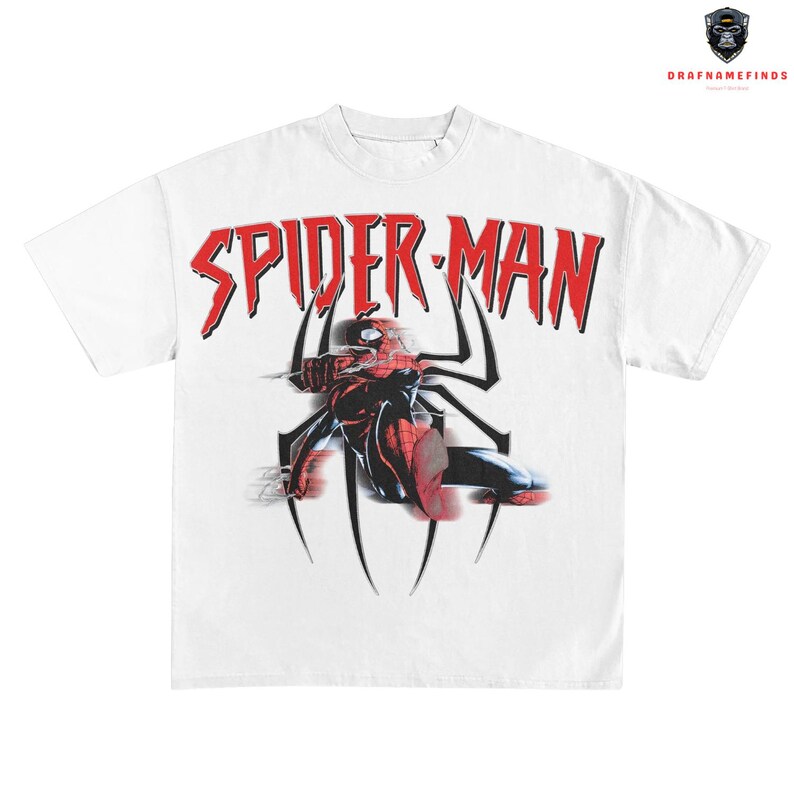 May include: White t-shirt featuring a graphic of Spider-Man in a dynamic pose, with the words "SPIDER-MAN" in red, stylized lettering. The design includes a black spider web and a red and black Spider-Man figure.
