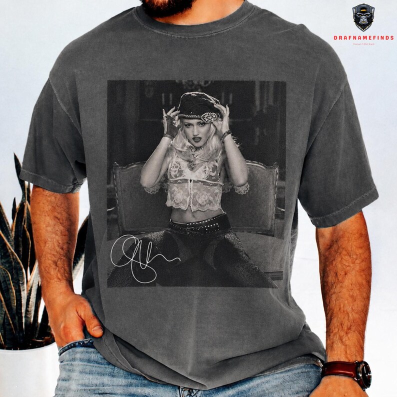 Peut inclure: T-shirt gris fonc&eacute; avec une image en noir et blanc d'une femme portant un chapeau et un haut en dentelle. L'image comprend une signature. Le t-shirt est de style vintage.
