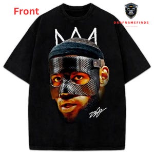 May include: Black t-shirt featuring a graphic of a person wearing a mask and a crown. The image has the text "Front" in the upper left corner and the text "DRAFNAMEFINDS" in the upper right corner. The graphic is in shades of black, brown, and white.