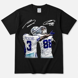May include: A black short-sleeve t-shirt featuring a graphic of two football players in white jerseys with blue numbers 3 and 88. The player with number 3 has the name PICKENS printed above the number. Two white signatures are printed above the players.