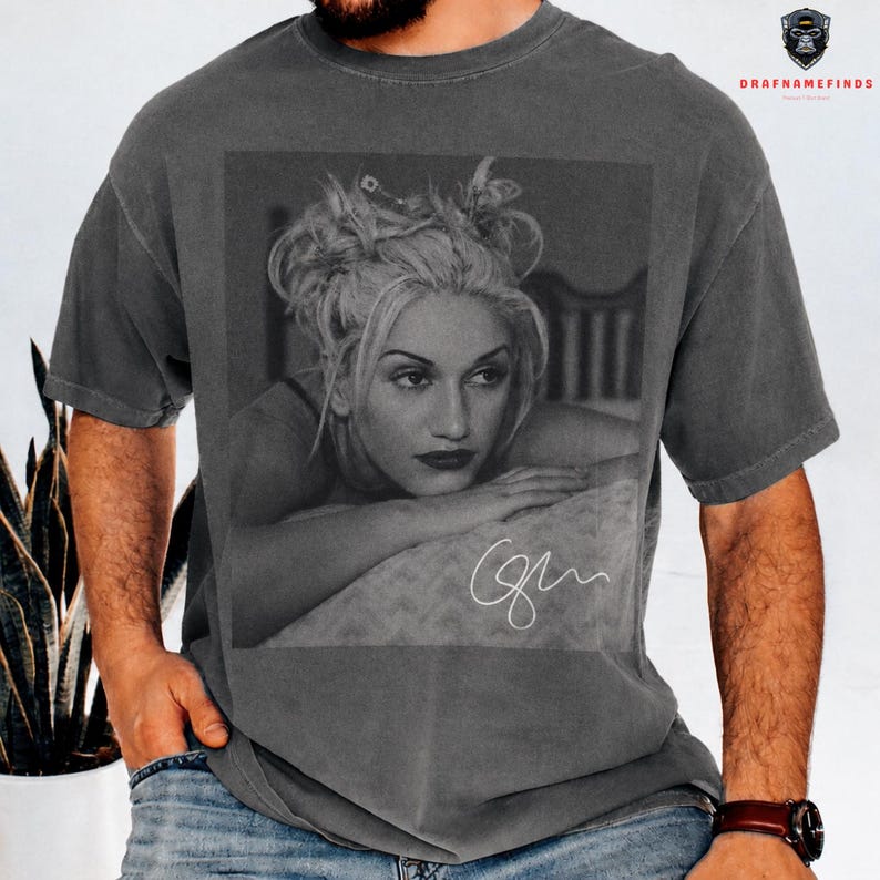 Peut inclure: T-shirt gris fonc&eacute; avec une image en noir et blanc d'une femme aux cheveux blonds et au rouge &agrave; l&egrave;vres rouge. L'image comprend une signature. Le t-shirt est de style vintage.