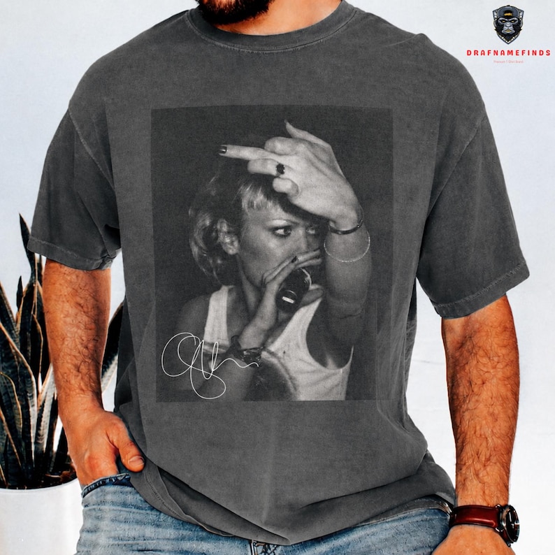 Peut inclure: T-shirt gris fonc&eacute; avec une image en noir et blanc d'une personne buvant &agrave; une bouteille et faisant un doigt d'honneur. L'image comprend une signature. Le t-shirt est port&eacute;.