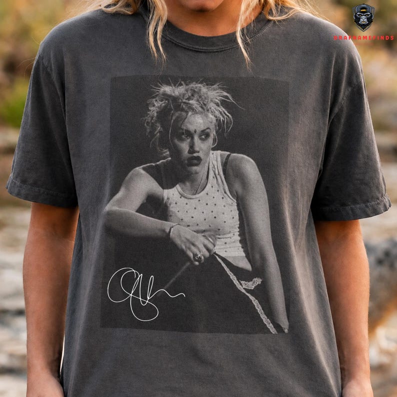 Peut inclure: T-shirt gris fonc&eacute; avec une image en noir et blanc d'une femme portant un d&eacute;bardeur blanc &agrave; pois. L'image comprend une signature. Le t-shirt a des manches courtes.