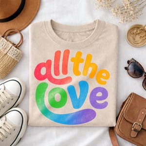 May include: A beige sweatshirt with the words "all the love" in rainbow colors. The sweatshirt is surrounded by a straw bag, sunglasses, a brown purse, a hat, and white sneakers.