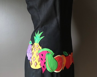 May include: A black linen dress with a colorful fruit embroidery design on the bottom hem. The embroidery includes a pineapple, watermelon, pear, orange, and apple.