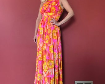May include: A woman wearing a long, sleeveless maxi dress with a floral print in shades of orange, pink, and yellow. The dress has a fitted bodice and a flowing skirt.