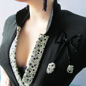 May include: A black cardigan with a floral trim and a black velvet bow with a black button in the center. The cardigan has a deep V-neckline.