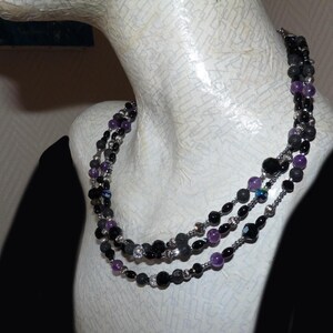 May include: A three-strand necklace with black, gray, and purple beads. The necklace is made of various materials, including lava rock, onyx, and amethyst.