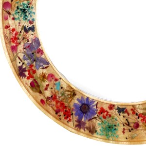 May include: A round wooden frame with a gold finish, decorated with pressed flowers and leaves in shades of red, pink, blue, green, and yellow.