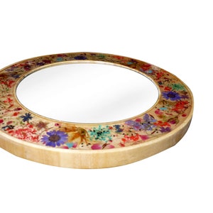May include: A round mirror with a wooden frame decorated with pressed flowers in shades of pink, purple, blue, green, and yellow.