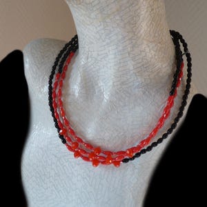 May include: A layered necklace with black and red beads. The necklace is made of oval-shaped beads and is worn on a white mannequin.