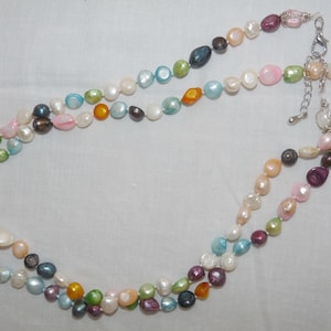 May include: A multi-strand pearl necklace featuring a range of colours, including white, pink, blue, green, and brown. The necklace is made from irregular shaped pearls and has a silver clasp.