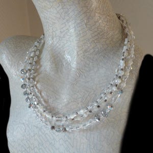 May include: A multi-strand necklace made of white and silver beads. The necklace is layered and features a variety of bead shapes and sizes.