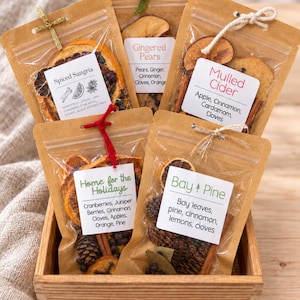 May include: Five kraft paper pouches containing dried fruit and spice blends for beverages, labeled Spiced Sangria, Gingered Pears, Mulled Cider, Home for the Holidays, and Bay Pine, arranged in a wooden crate with decorative string ties.