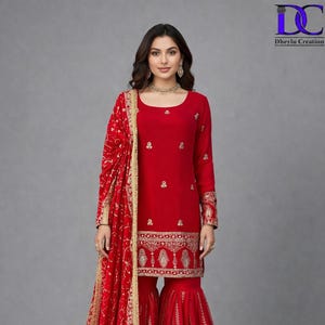 Può includere: Un vivace completo rosso con un top a maniche lunghe e pantaloni svasati, adornato da intricati ricami dorati. Una sciarpa abbinata con finiture dorate completa l'outfit. L'abbigliamento è di stile tradizionale.