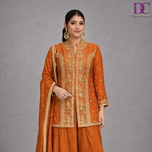 May include: An orange-colored, three-piece ensemble featuring a long-sleeved jacket with intricate gold embroidery, a matching wide-leg skirt, and a sheer scarf. The jacket has a mandarin collar and is adorned with detailed floral patterns. The outfit is suitable for special occasions.