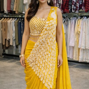 May include: A vibrant yellow sleeveless blouse and matching skirt ensemble featuring intricate white embroidery. The bodice has a textured pattern with dangling beads, while the skirt displays a prominent white leaf-shaped applique design.
