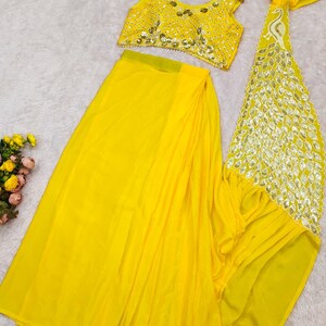 May include: A bright yellow two-piece outfit consisting of a sleeveless crop top and a long skirt. The top features intricate gold-toned embroidery and mirror-like embellishments. A matching yellow dupatta with a decorative peacock-shaped border.