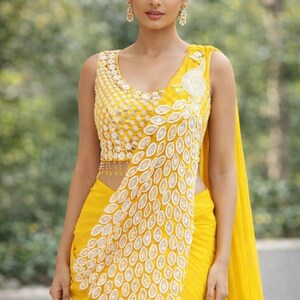 May include: A bright yellow sleeveless blouse and matching saree featuring intricate white embroidery in a repeating leaf pattern. The bodice displays dense floral stitching, while the drape showcases a prominent peacock-inspired motif.