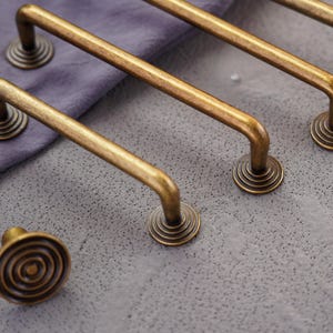 Puede incluir: Juego de herrajes de gabinete de latón antiguo. Incluye varios tiradores y un solo pomo. Los tiradores tienen un diseño curvo con una base circular. El pomo tiene un diseño en espiral. El herraje es de metal y tiene un aspecto vintage.