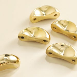 May include: Six polished brass cabinet pulls with a smooth, curved design. Each pull has two screw holes and a reflective surface, creating a warm, golden glow. These hardware pieces are ideal for adding a touch of elegance to furniture.