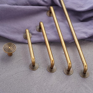 May include: A collection of antique brass cabinet hardware, including a knob and several pull handles of varying lengths. The hardware features a circular design on the base and a warm, aged finish, suggesting a vintage aesthetic.