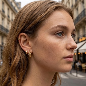 Peut inclure: Un ensemble de trois boucles d'oreilles dorées comprenant un petit ear cuff placé sur le cartilage supérieur et deux créoles lisses en forme de goutte de tailles différentes portées au lobe, le tout avec une finition polie et brillante.